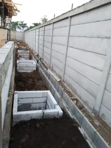 Parit drainase digali sepanjang dinding pembatas beton pracetak, dengan bak kontrol dari pasangan bata di dalamnya.