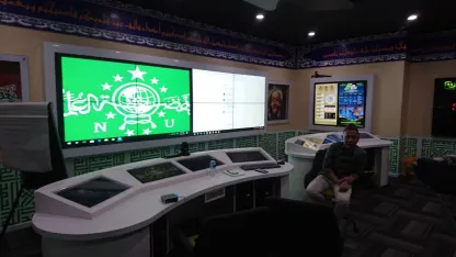 Ruang kendali yang sama dilihat dari samping, sebuah logo memenuhi video wall dan satu orang duduk di meja samping.