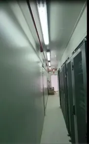 Lorong sempit di dalam kontainer dengan pintu rak berwarna gelap tertutup rapat di satu sisinya.