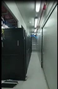Kabinet perangkat berdiri di satu sisi lorong kontainer, dengan pipa pemadam merah membentang di atasnya.