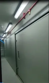 Pipa sprinkler dengan kepala pemancar terpasang di bawah langit-langit kontainer, melewati pintu peralatan yang lebar.