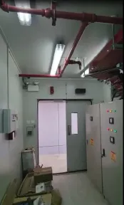Pipa pemadam merah, bel alarm, dan panel kontrol di samping pintu ganda kontainer.