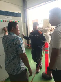Seorang teknisi menekan tombol di muka panel sementara dua rekannya mengamati dari balik rantai pembatas.