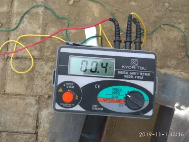 Alat uji pembumian digital tergeletak di tanah menunjukkan 0,4 ohm, kabel ujinya terjepit pada elektroda yang sedang diukur.
