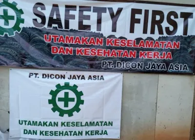 Dua spanduk keselamatan bertuliskan Safety First dan Utamakan Keselamatan dan Kesehatan Kerja, keduanya mencantumkan nama perusahaan.