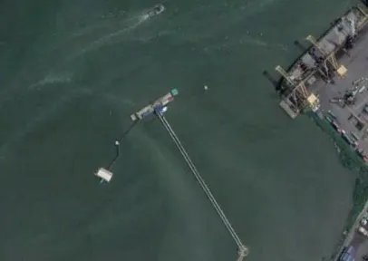Foto satelit trestle panjang yang menjorok ke laut menuju dermaga, dengan quay berderek di salah satu sisinya.