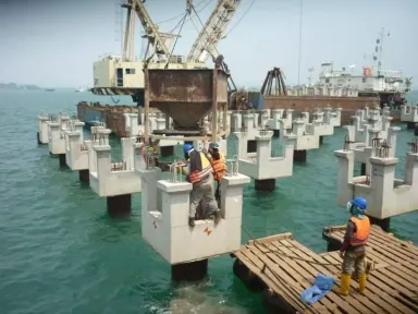 Seorang pekerja memanjat kepala tiang saat derek mengayunkan bak beton di atas barisan tiang pancang.