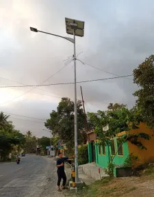 Lampu jalan tenaga surya di tiangnya di tepi jalan desa, dengan seorang teknisi berdiri di kaki tiang.